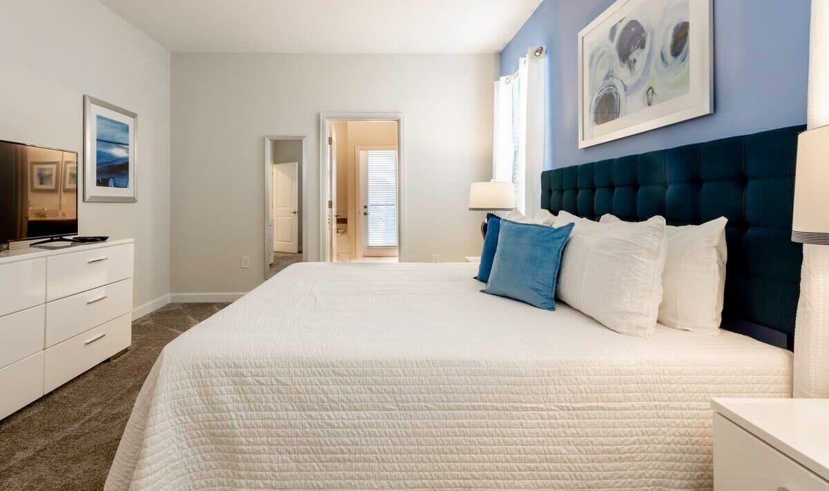 A bedroom with a large bed, a dresser, a TV, and artwork on the walls.