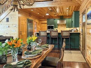 Un intérieur en bois comprenant une table à manger pour quatre personnes, un coin cuisine et un escalier.