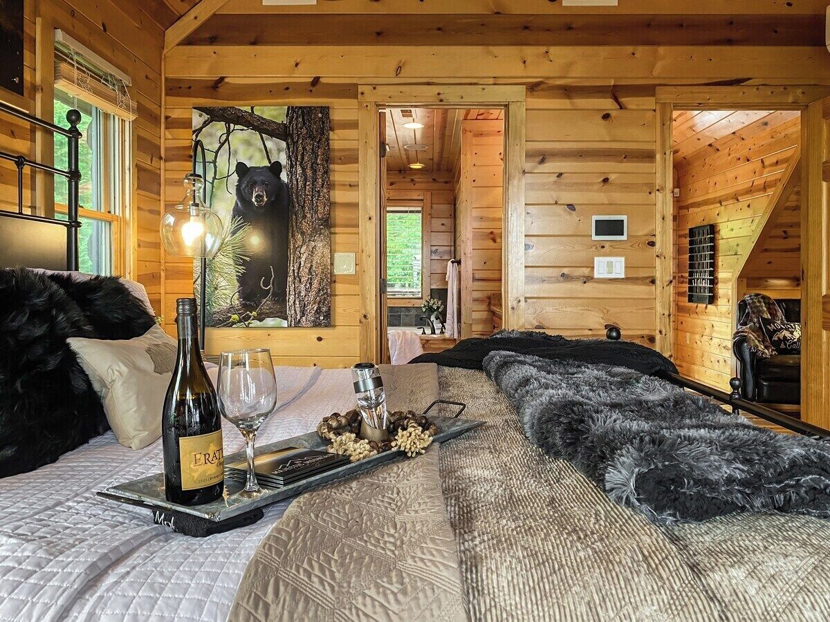 A cozy log cabin room with a bed, a wine bottle, and glasses on a tray.