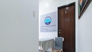 Una habitación con una puerta de madera marcada con el número 5, una mesa con mantel estampado y una silla con cojín gris.