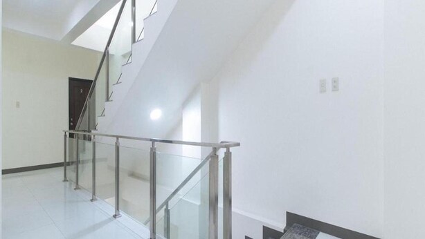Un interior moderno con barandilla de vidrio en una escalera, paredes blancas y suelo de baldosas.