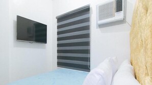 Una habitación con una cama, televisor, ventana con persianas y aire acondicionado.