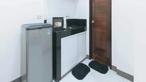 Una kitchenette compacta con refrigerador, microondas y un estante pequeño sobre la encimera.
