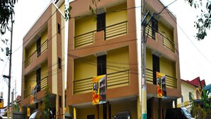 Un edificio de varios pisos con fachada amarilla, varios balcones y un estacionamiento con varios vehículos.