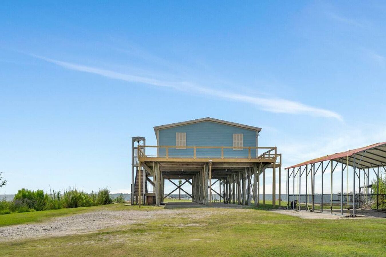 A two-story wooden structure with a balcony, elevated on stilts, overlooking a body of water.