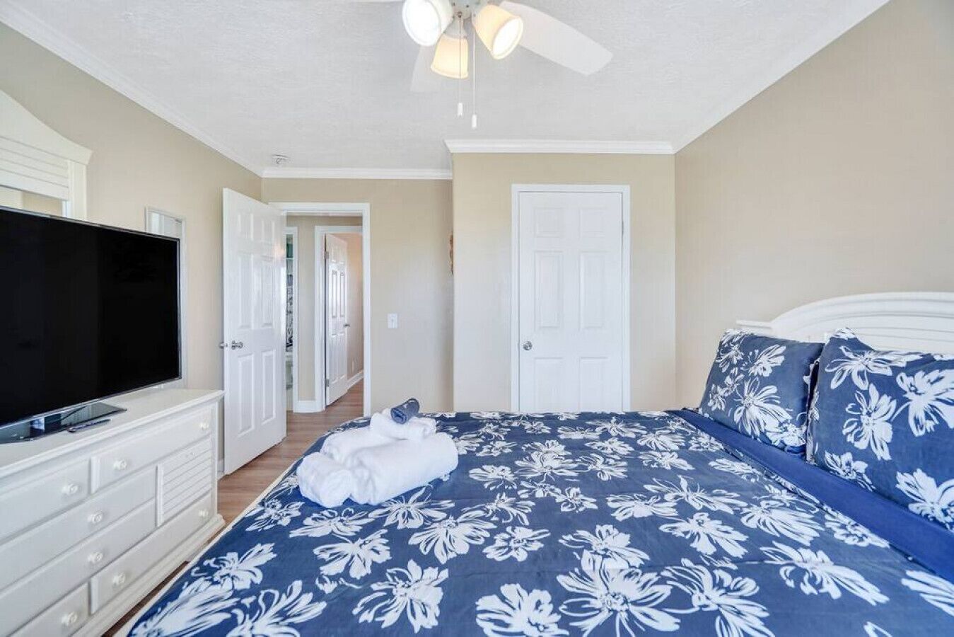 A bedroom with a bed, a TV, a ceiling fan, and a door.