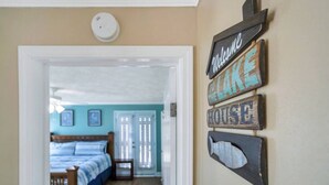 A hallway leading to a bedroom with a bed, a wall-mounted sign, and a smoke detector. - Family Friendly Waterfront Home | Private backyard (New Orleans)