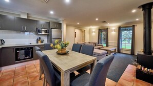 Eine moderne Küche mit dunklen Schränken und Edelstahlgeräten, ein Essbereich mit Holztisch und blauen Stühlen sowie ein gemütlicher Wohnbereich mit einer Couch und Kamin.
