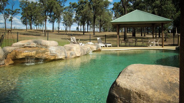 Ein klares Schwimmbecken mit Felsen, einem Pavillon und Liegestühlen.