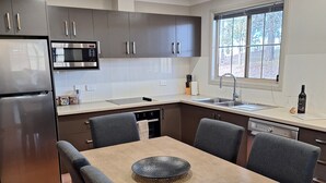 Eine moderne Küche mit integriertem Mikrowellenherd, Edelstahlkühlschrank und Essbereich mit Holztisch und Stühlen.