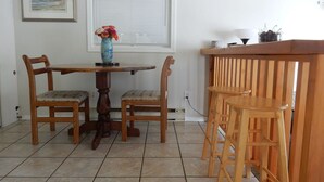 A dining area with a wooden table and chairs, a vase with flowers, and a window with blinds. - Beautiful Beach front cottage near Nelson, BC (Nelson)