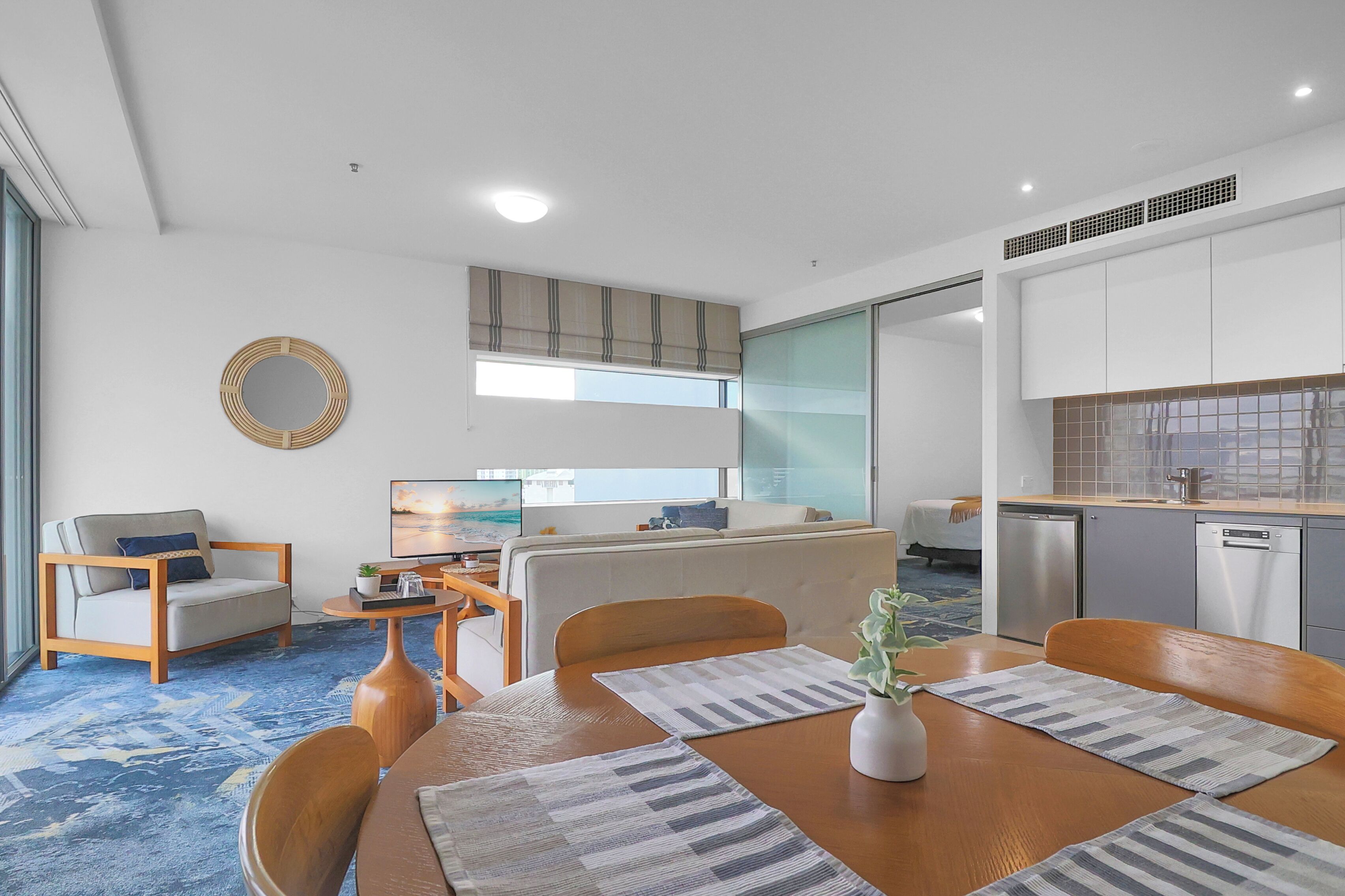 A modern hotel room with a dining area, kitchenette, and a large window.