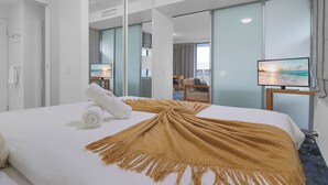 Une chambre d’hôtel avec un grand lit, une télévision, un bureau et une vue sur la mer par la fenêtre.