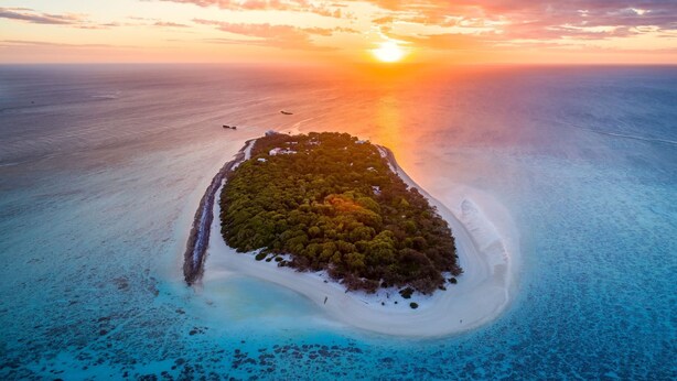 Vue aérienne d’une île tropicale, avec un ciel dégagé et un coucher de soleil.