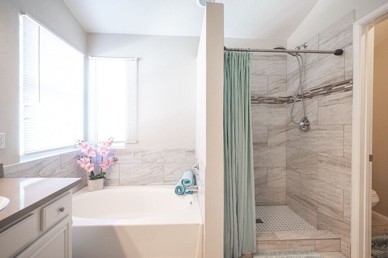 Une salle de bain avec une baignoire, une douche et une fenêtre équipée de stores.