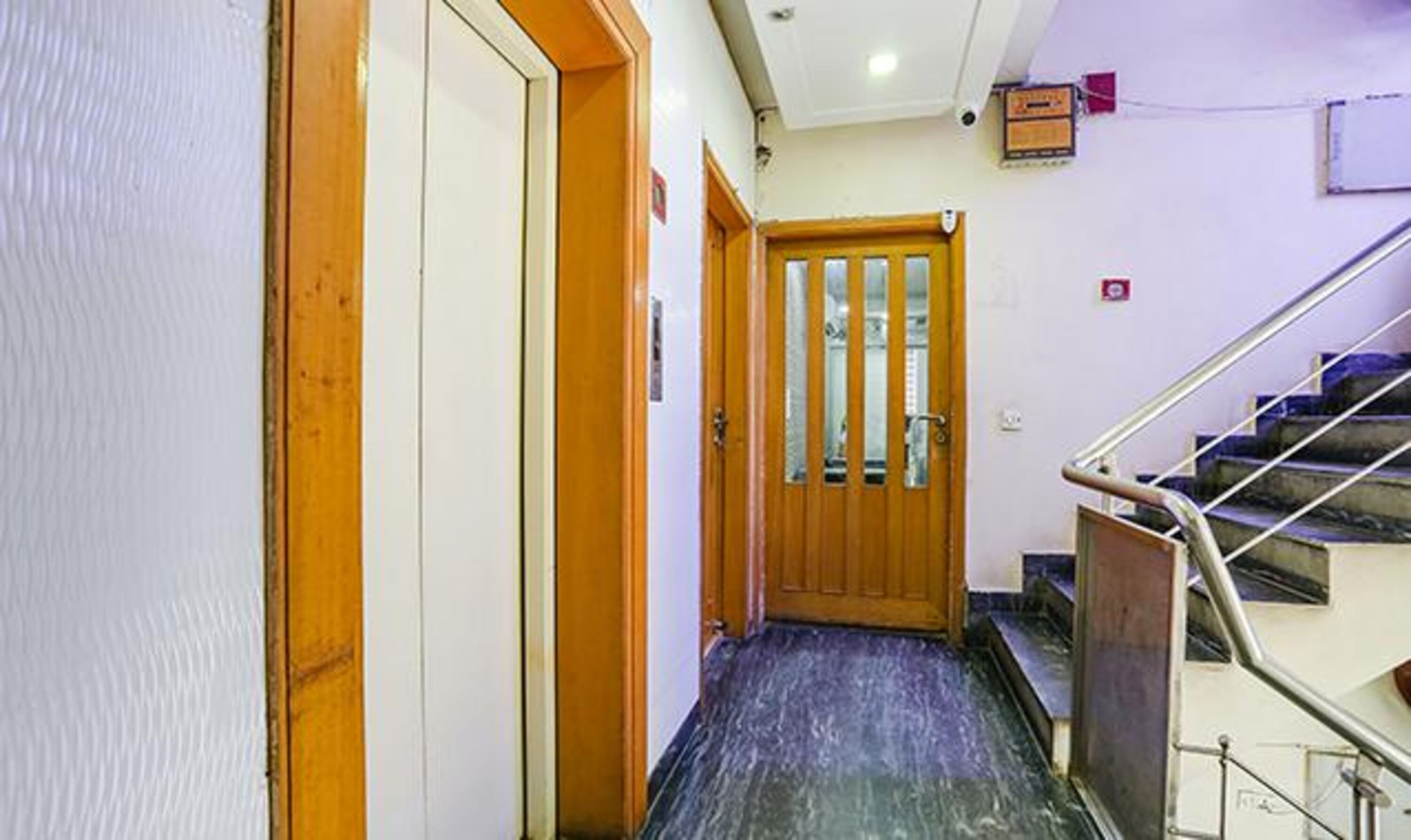 A hallway with wooden doors, a marble floor, and a staircase with metal railings.