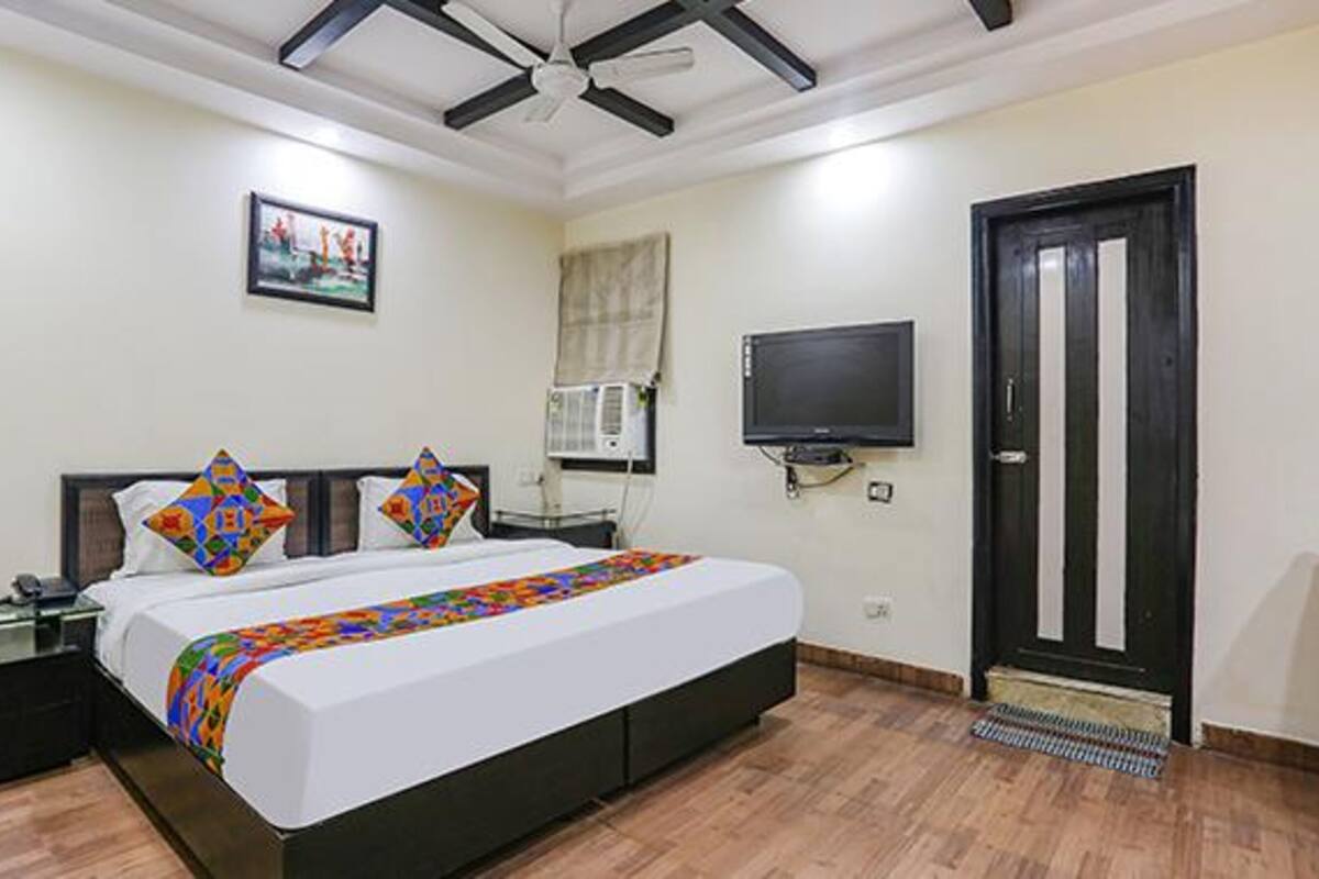 A hotel room with a bed, a TV, an air conditioning unit, and a door.