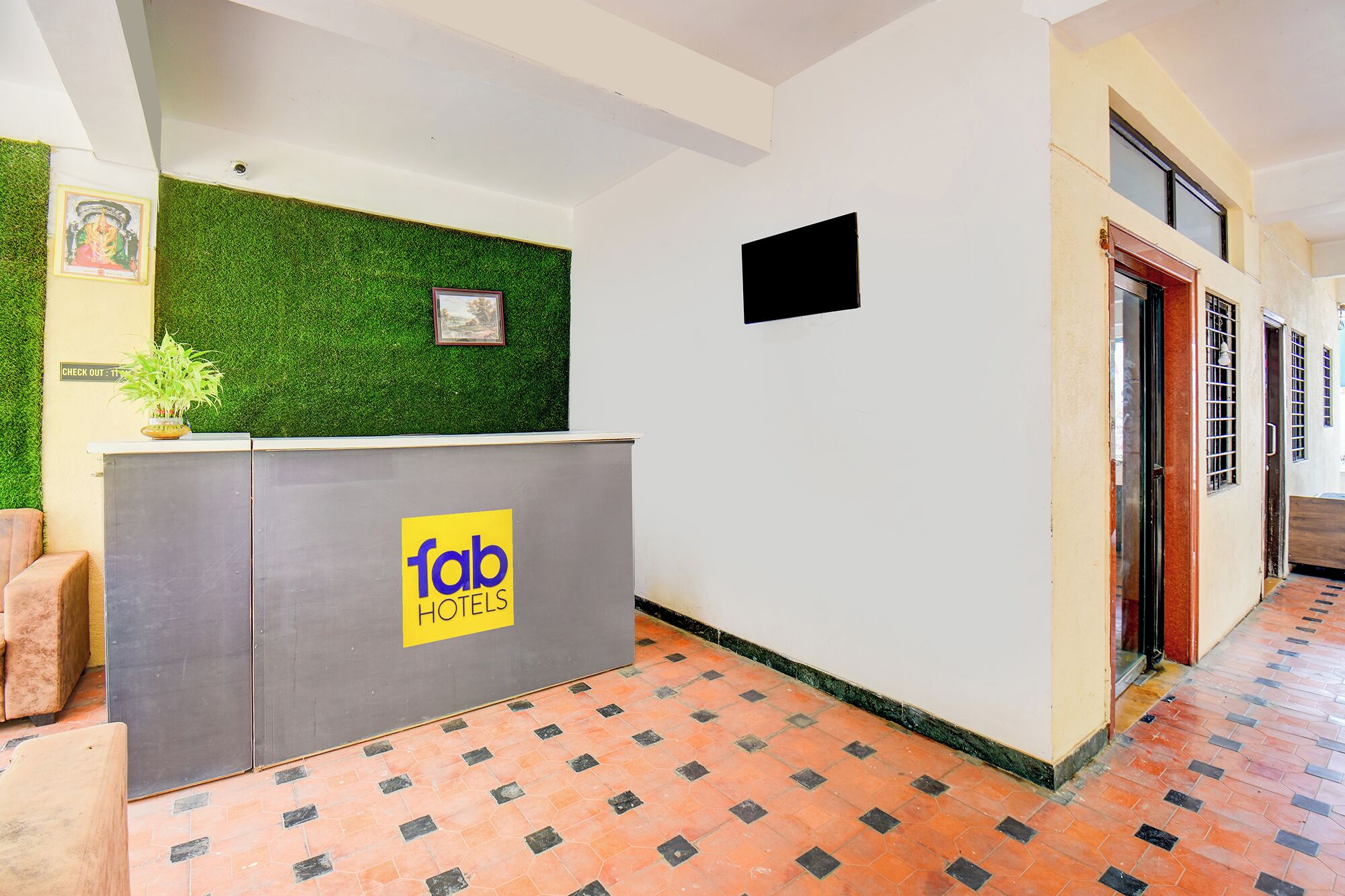 Egy fogadótér, ahol a kijelentkezéshez tartozó tábla található, egy zöld fal, amelyen egy kép van, és egy tábla, amelyen a „fab hotels” felirat szerepel.