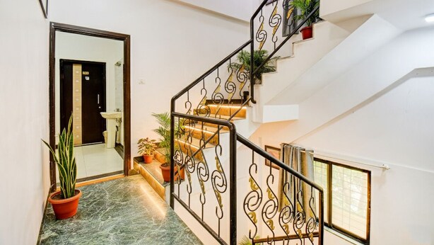 Una escalera con barandillas metálicas ornamentales, plantas en macetas y vista al baño.