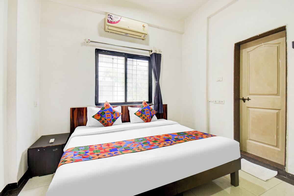 Un dormitorio con cama, ventana con cortinas, equipo de aire acondicionado y puerta de madera.