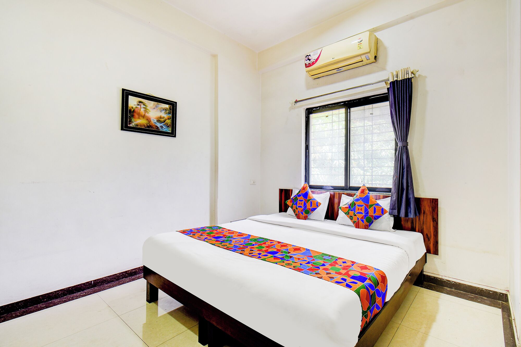 A bedroom with a bed, a window with curtains, an air conditioning unit, and a framed picture on the wall.