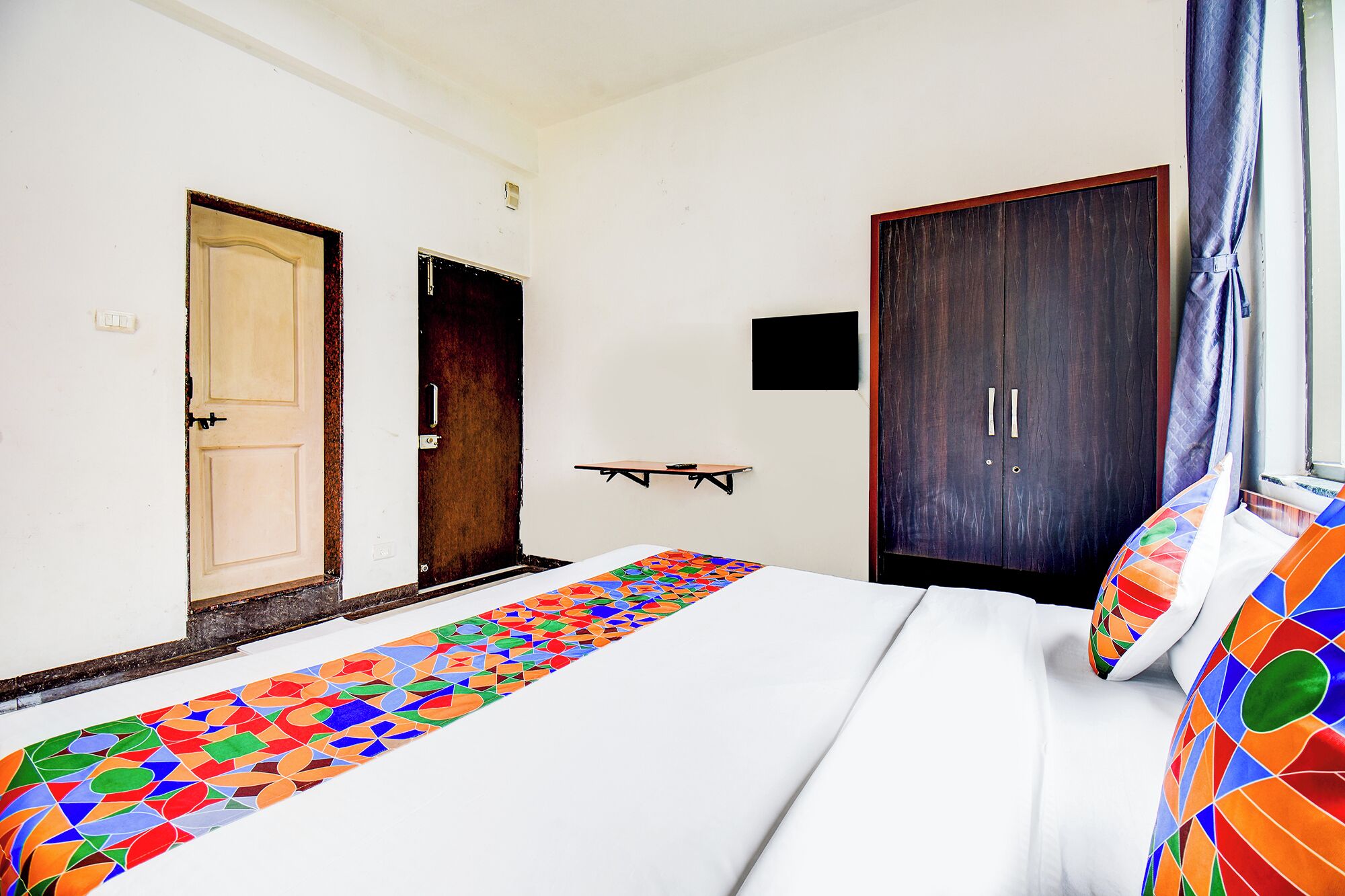 A hotel room with a bed, a small table, a wardrobe, and a door.