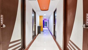 A hotel corridor with a push button on the doors, a tiled floor, and a modern ceiling design. - Fabhotel Blue Moon I (Ahmedabad)