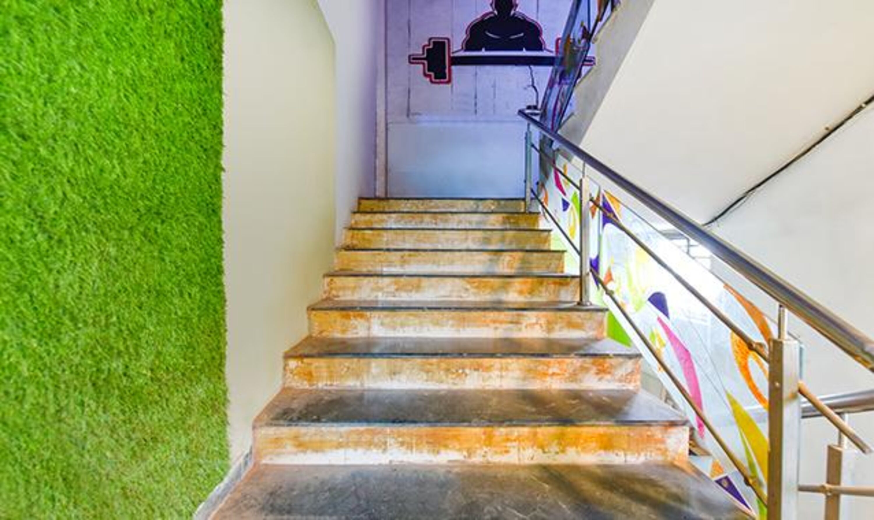 Una escalera con barandilla metálica y una pared verde a un lado.