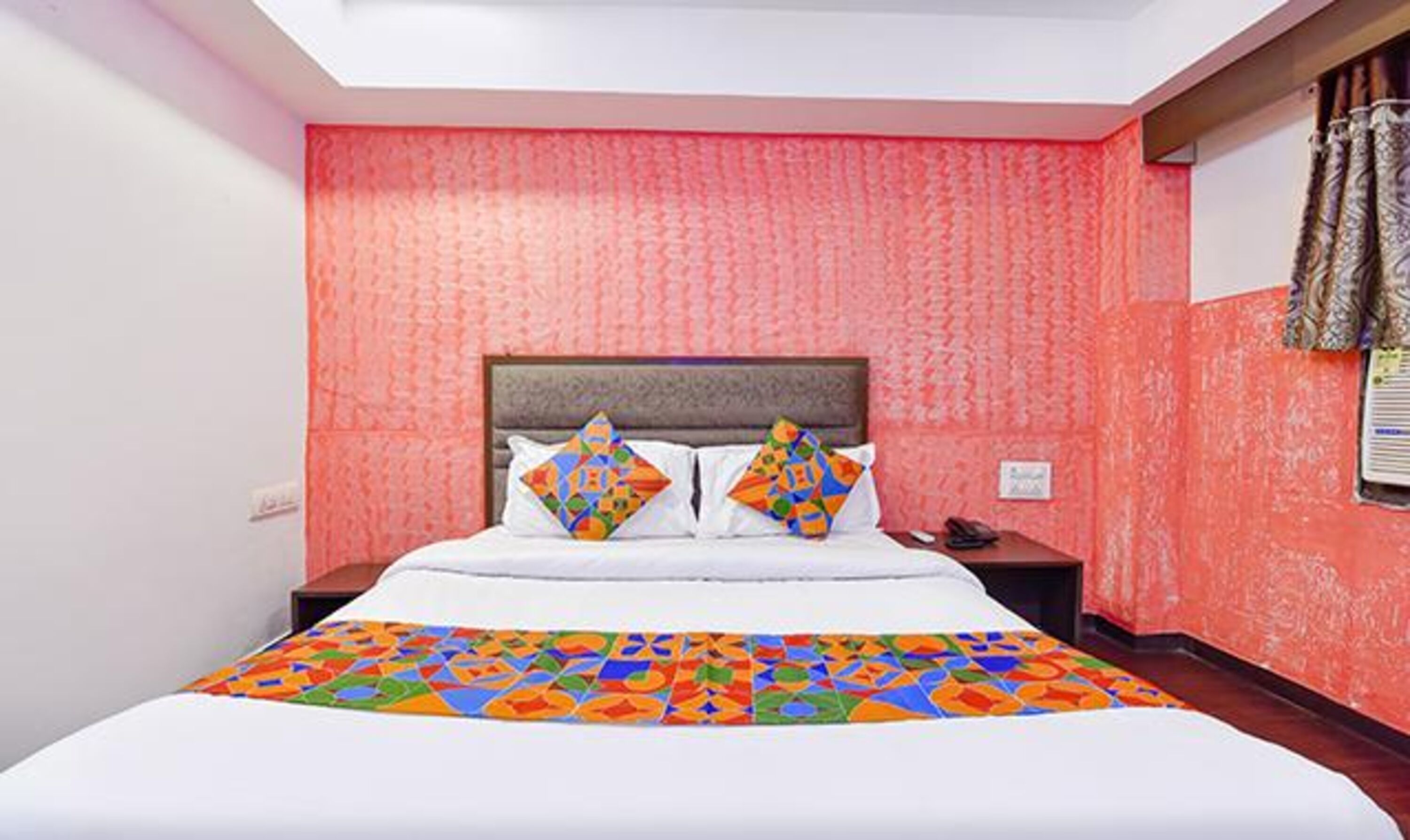 Quarto de hotel com cama grande, cabeceira, mesa de cabeceira e janela com cortinas.