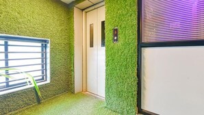 A hallway with green artificial grass walls, a door, and a window with blinds. - Fabhotel Blue Moon I (Ahmedabad)