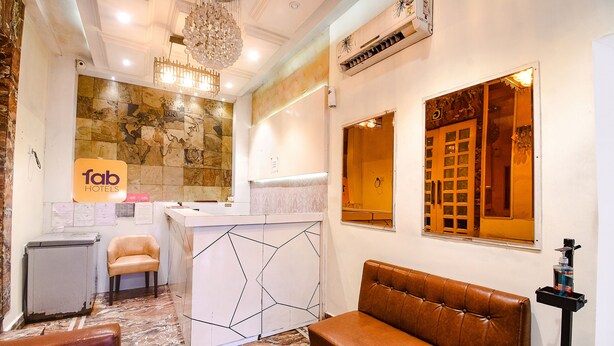 A hotel reception area with a marble floor, a reception desk, a brown leather sofa, and a chandelier. - Fabhotel Abis Inn (Kolkata)