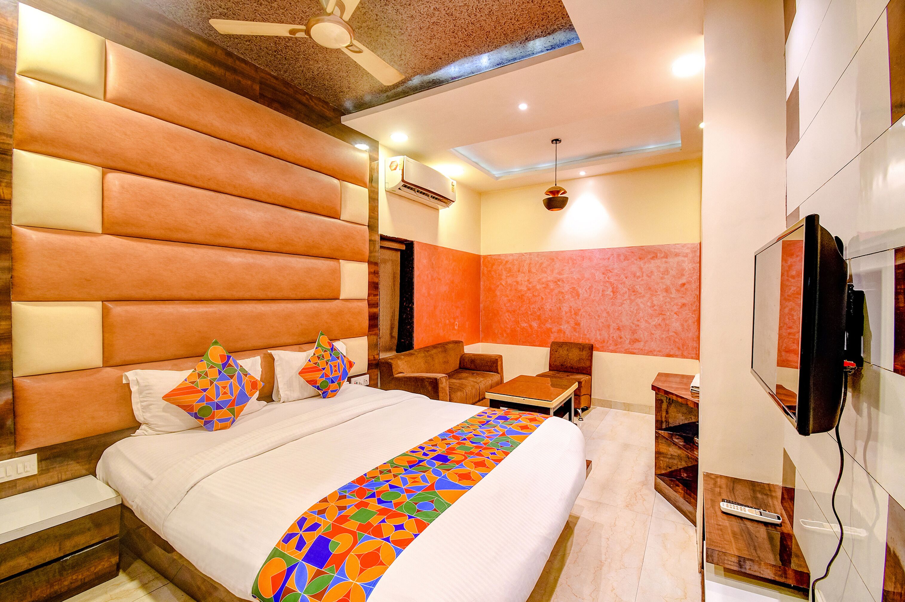 A hotel room with a large bed, a TV, a ceiling fan, and a small seating area.