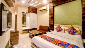A hotel room with a bed, a desk, a sofa, a mirror, and an air conditioning unit. - Fabhotel Abis Inn (Kolkata)