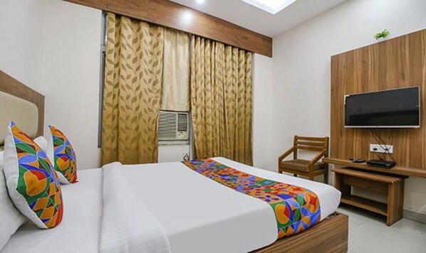 A hotel room with a bed, a desk, a chair, a television, and a window with curtains.