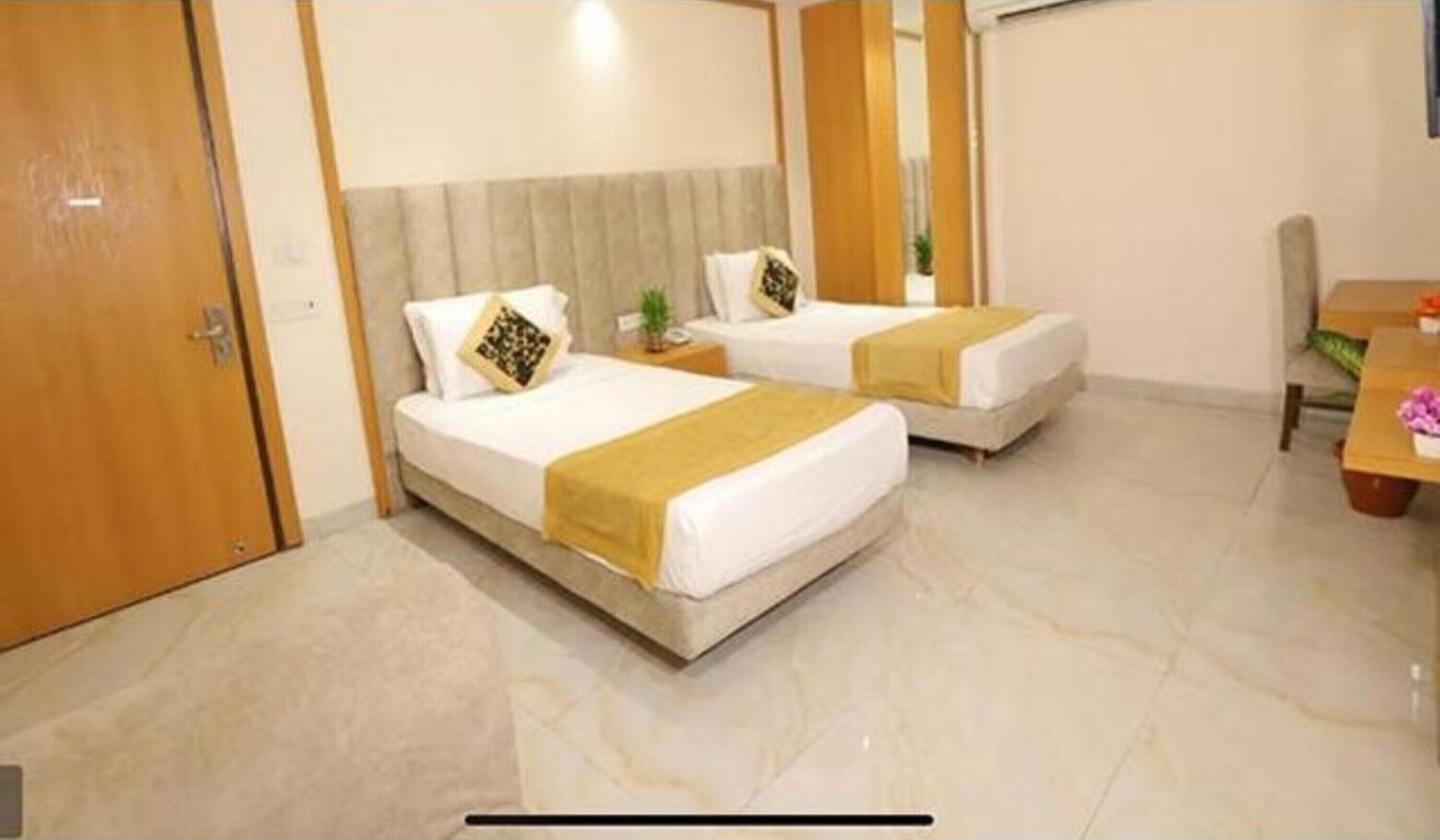 A hotel room with two beds, a wooden door, a small table with a plant, and a view of the outside.