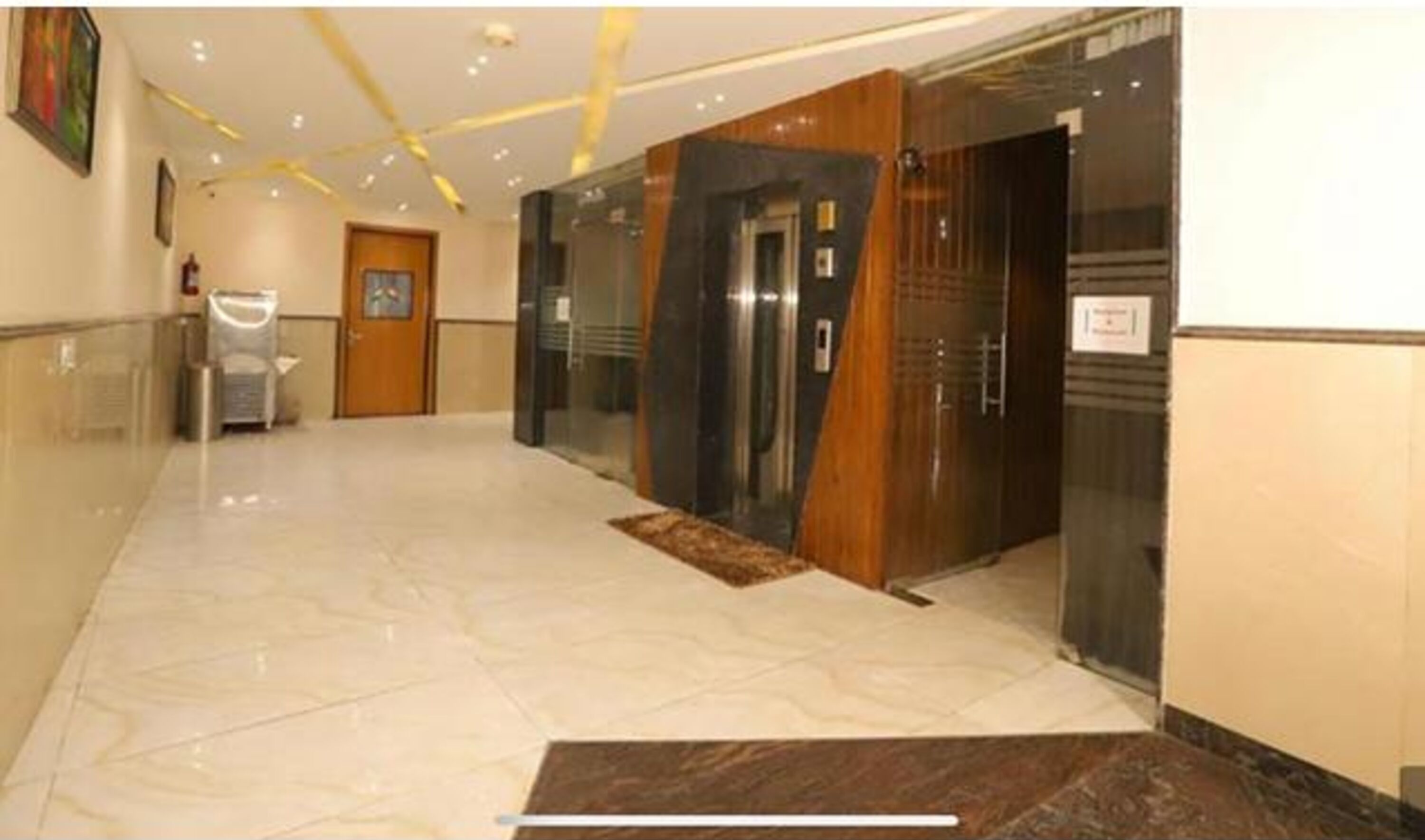 A hotel corridor with a marble floor, wooden paneling, and a glass elevator.
