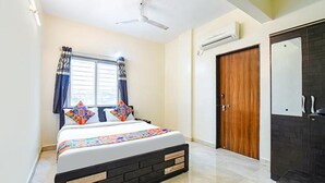 Une chambre à coucher avec un lit, une fenêtre avec des rideaux, un ventilateur de plafond, un appareil de climatisation et une porte en bois.