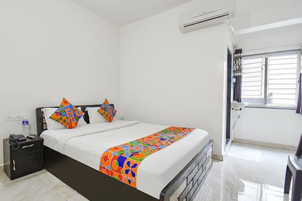A bedroom with a bed, a nightstand, a suitcase, and a window with blinds.