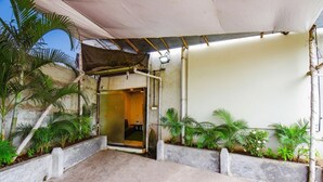Un espace extérieur abrité, doté d’un sol en béton, d’une porte donnant sur l’intérieur et agrémenté de plantes en pot.