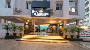 The entrance of Hotel The SunRise Inn with a welcoming sign, potted plants, and a well-lit pathway leading to the reception area.