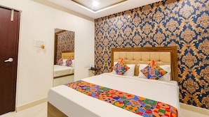A hotel room with a large bed, a wooden headboard, a patterned wallpaper, and a door.