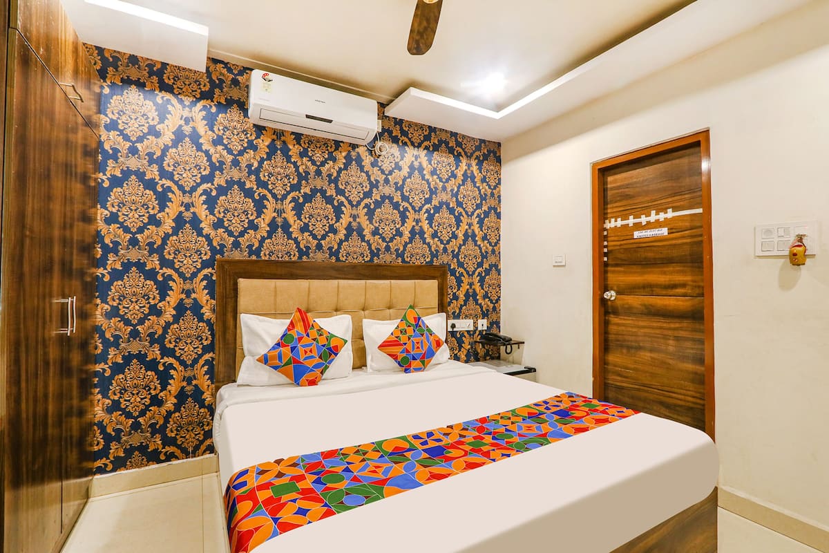 Ein Hotelzimmer mit strukturierter Tapete, einem Bett mit bunten Kissen, einer Holztür und einer Klimaanlage an der Wand.