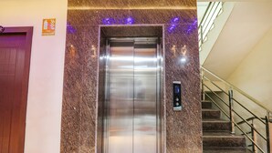 An elevator with a fire extinguisher sign above it, a control panel, and a staircase with metal railings.