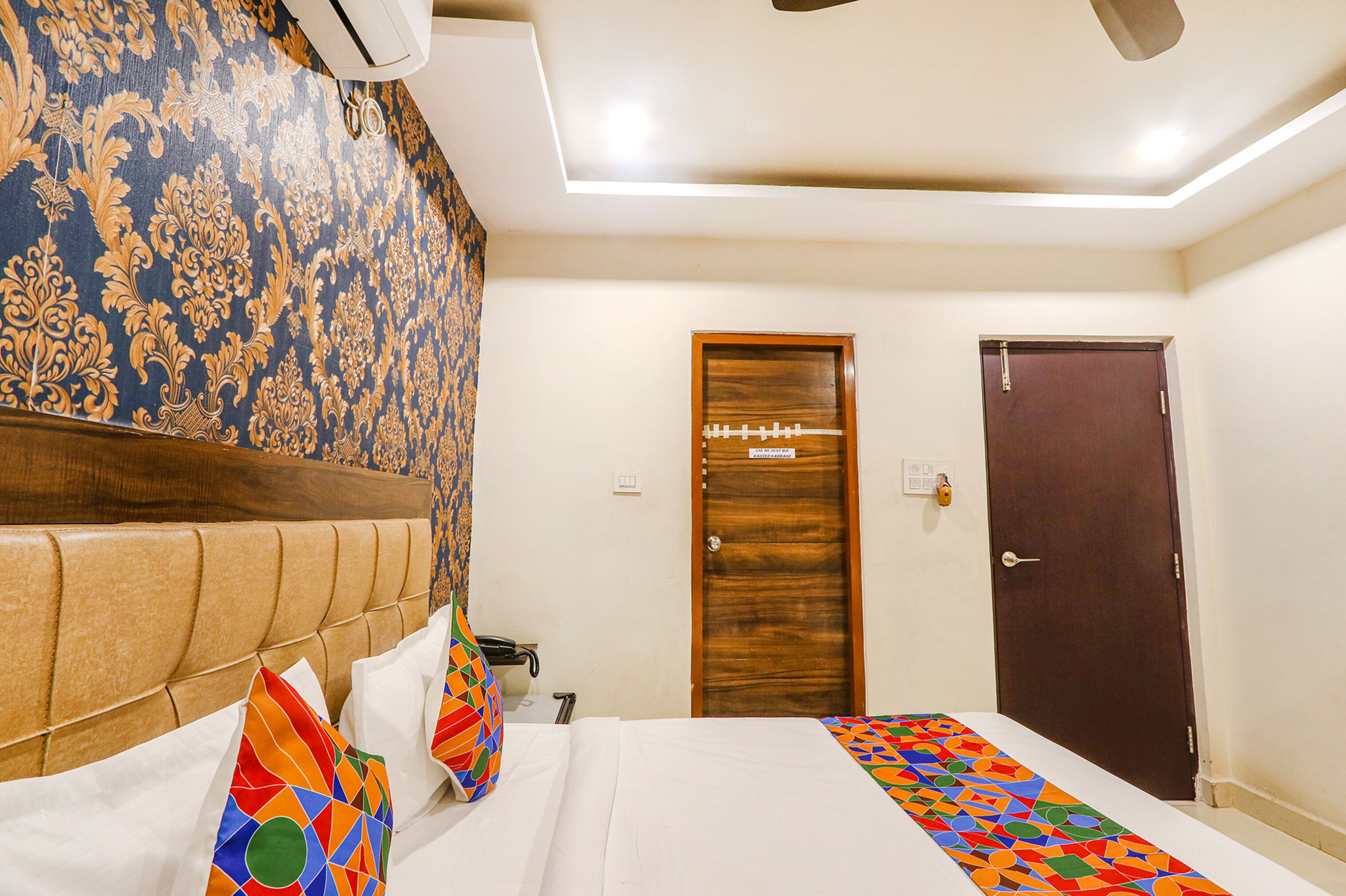 A hotel room with a large bed, a wooden headboard, a patterned wall, and a door.