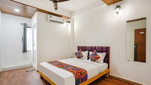 A bedroom with a bed, a ceiling fan, an air conditioning unit, a wooden door, and a window with a curtain.