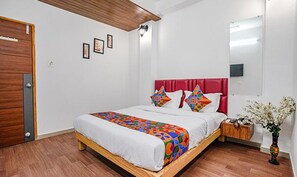 A bedroom with a wooden bed frame, a red headboard, and a colorful quilt. There is a nightstand with a vase of flowers and a wall-mounted lamp. - Fabexpress Silk (Surat)