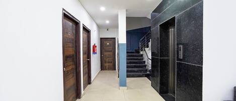 Un couloir moderne avec des portes en bois, un pilier bleu et un escalier agrémenté d’un mur en marbre.