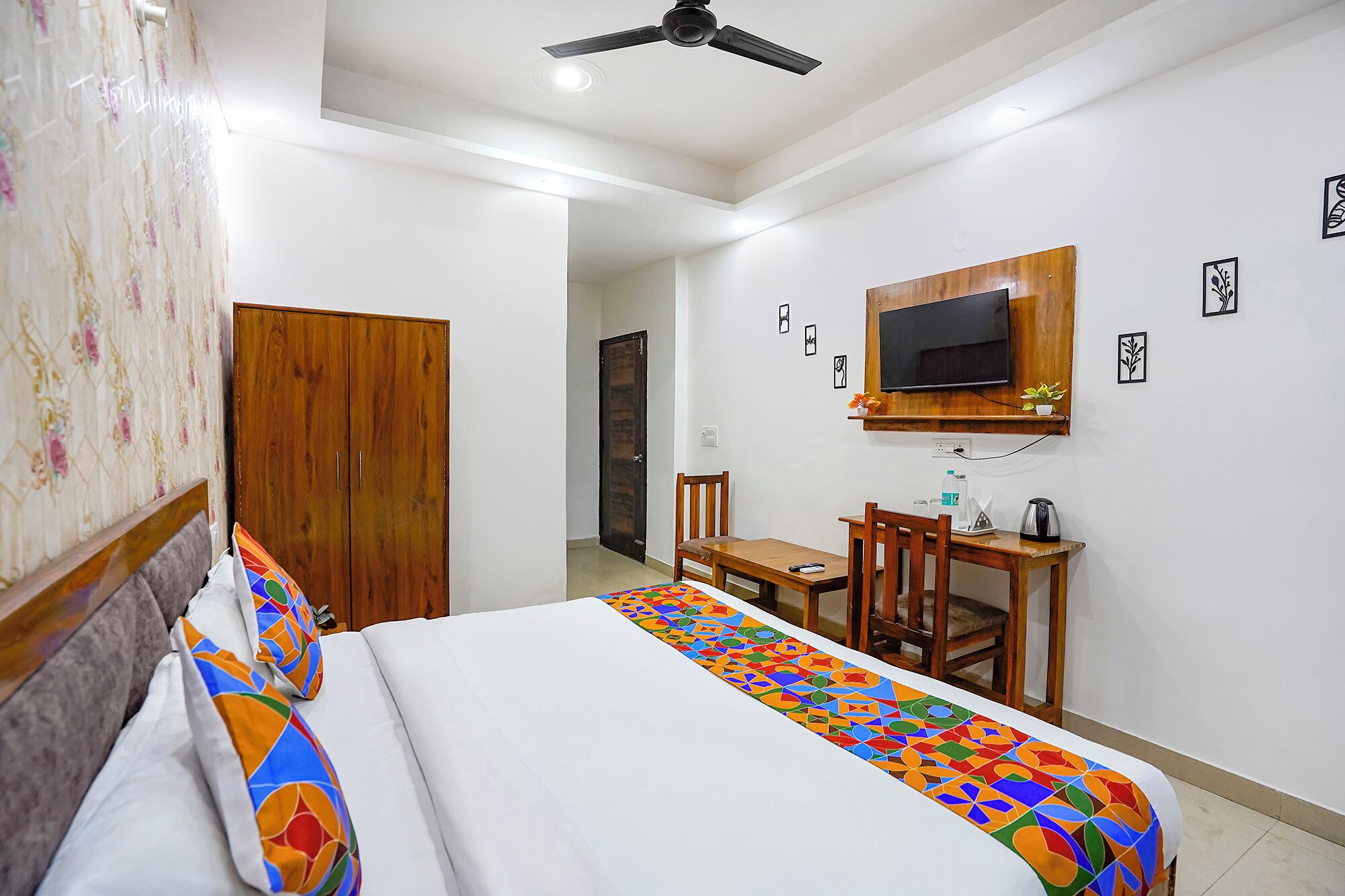 Habitación de hotel con cama, un escritorio con silla, televisor montado en la pared y una puerta que da a otra habitación.