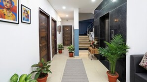 A hallway with wooden doors, potted plants, a staircase, and a grey rug. - FabHotel Frolic Luxury Stay (Noida)