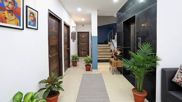A hallway with wooden doors, potted plants, a staircase, and a grey rug.
